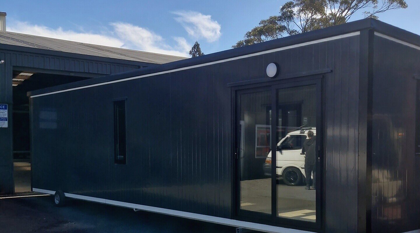 A 10 × 3 m charcoal Simple Cabins cabin with a ranch slider, in the Bell Block yard