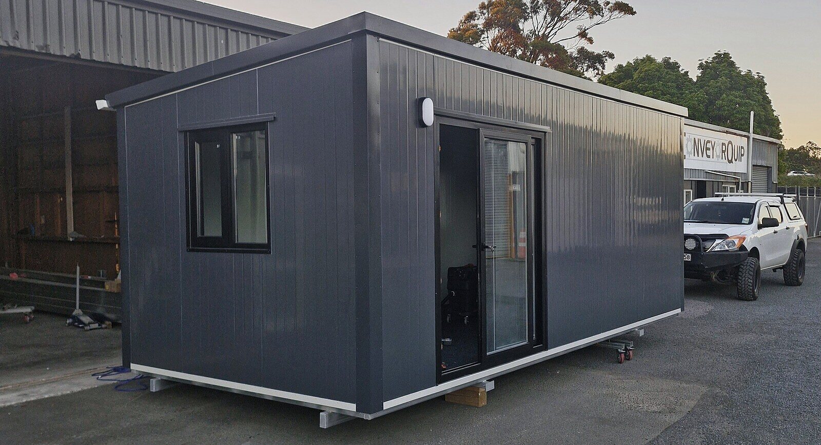 A 6 × 3 m charcoal Simple Cabins cabin with a window and ranch slider, outside the Bell Block workshop