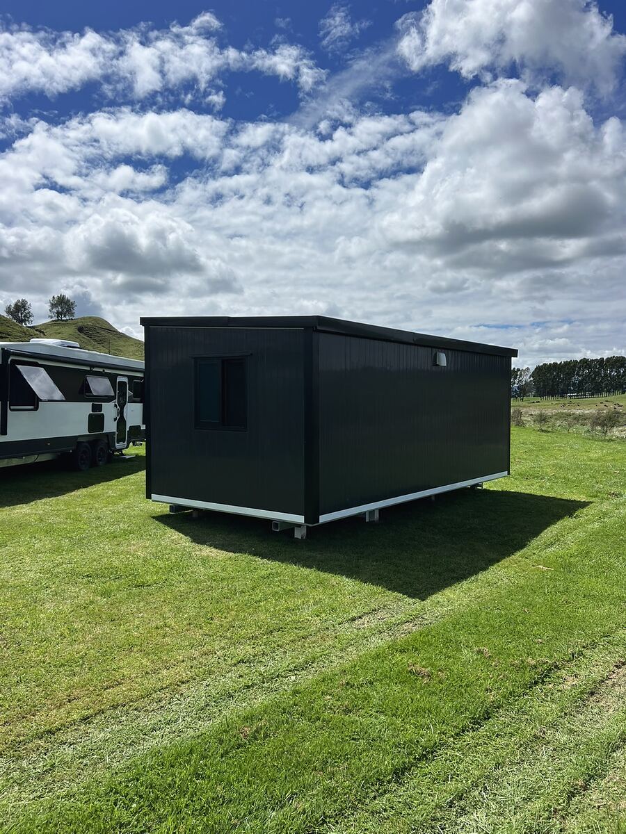A finished charcoal cabin standing on a lawn under a big Taranaki sky