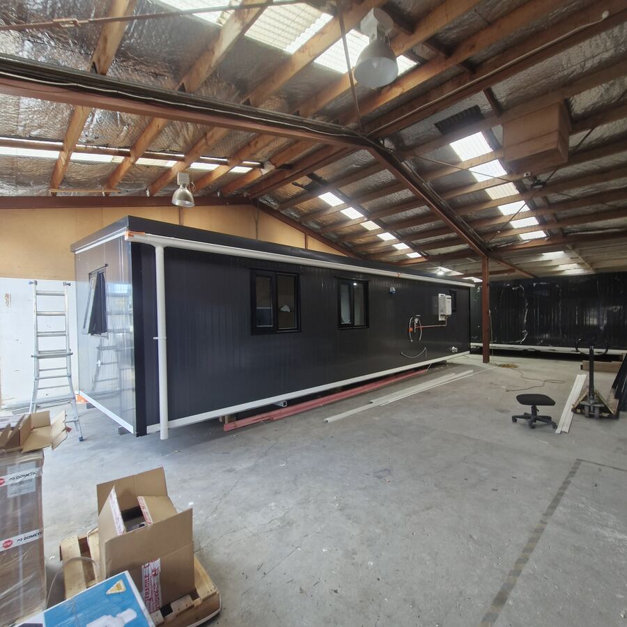 A long charcoal cabin with awning windows, being finished in the workshop