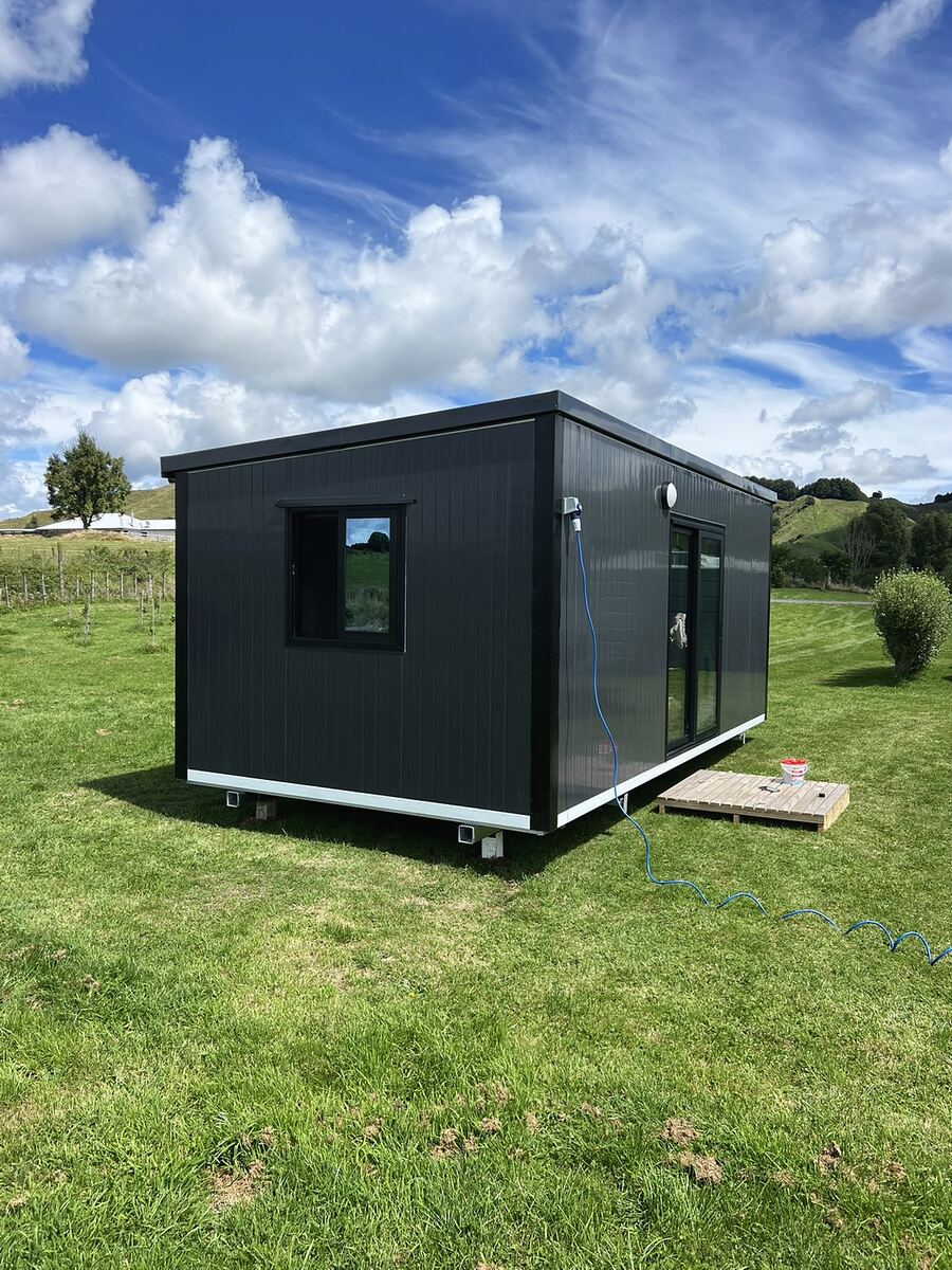 A 6 × 3 m black cabin with a window and ranch slider, sited on a lawn in the sun