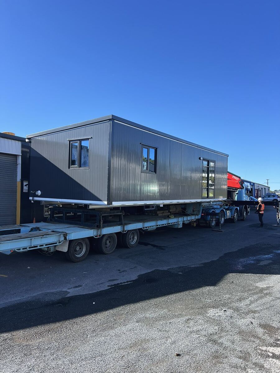 A cabin loaded on a trailer in the yard under a clear blue sky