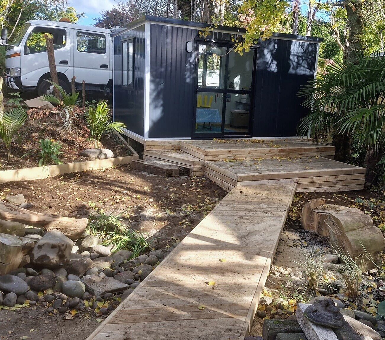 A cabin in a garden with a two-level timber deck and a boardwalk to the door
